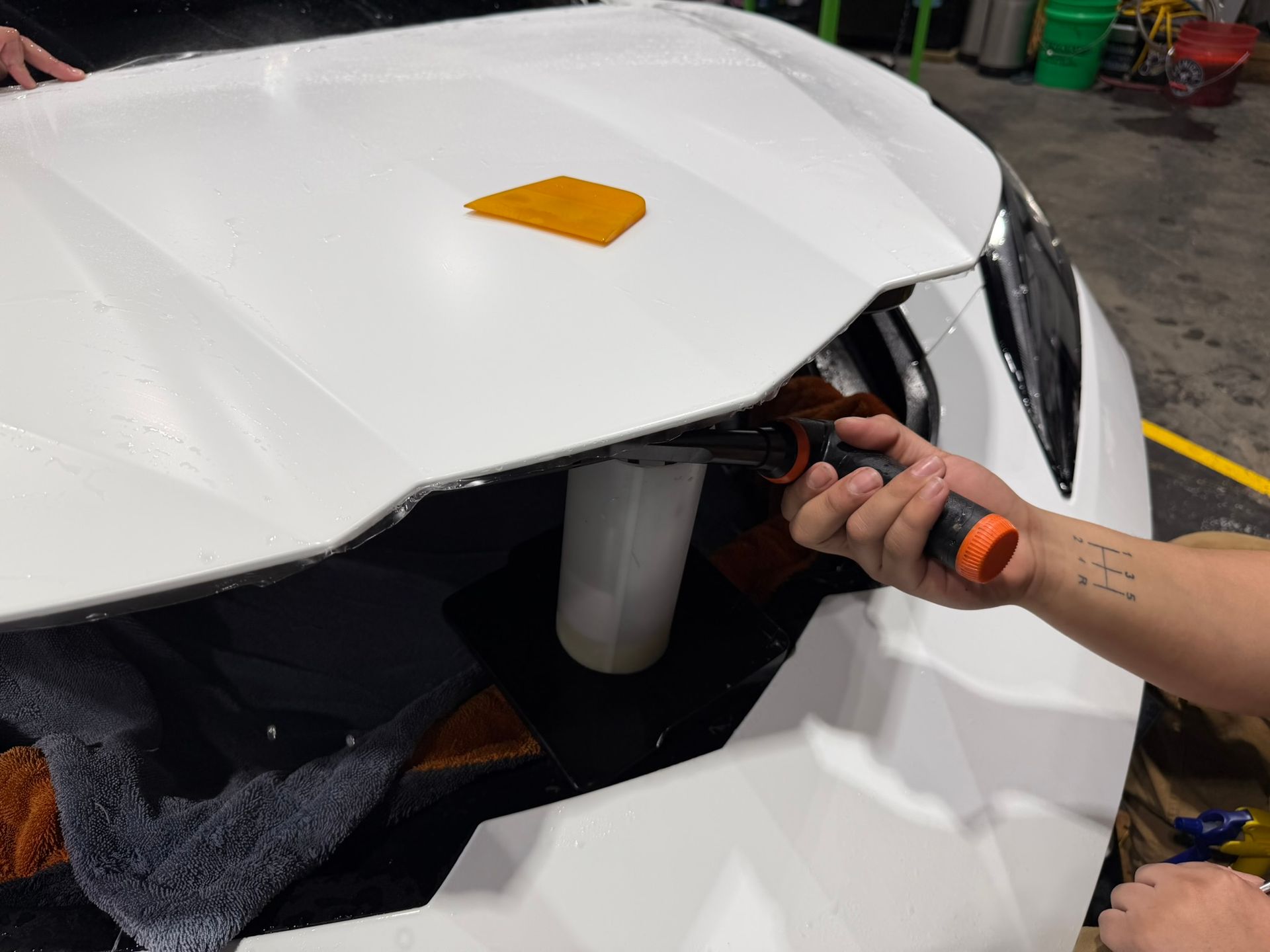 Person using a screwdriver to remove the front headlight of a white car in a garage
