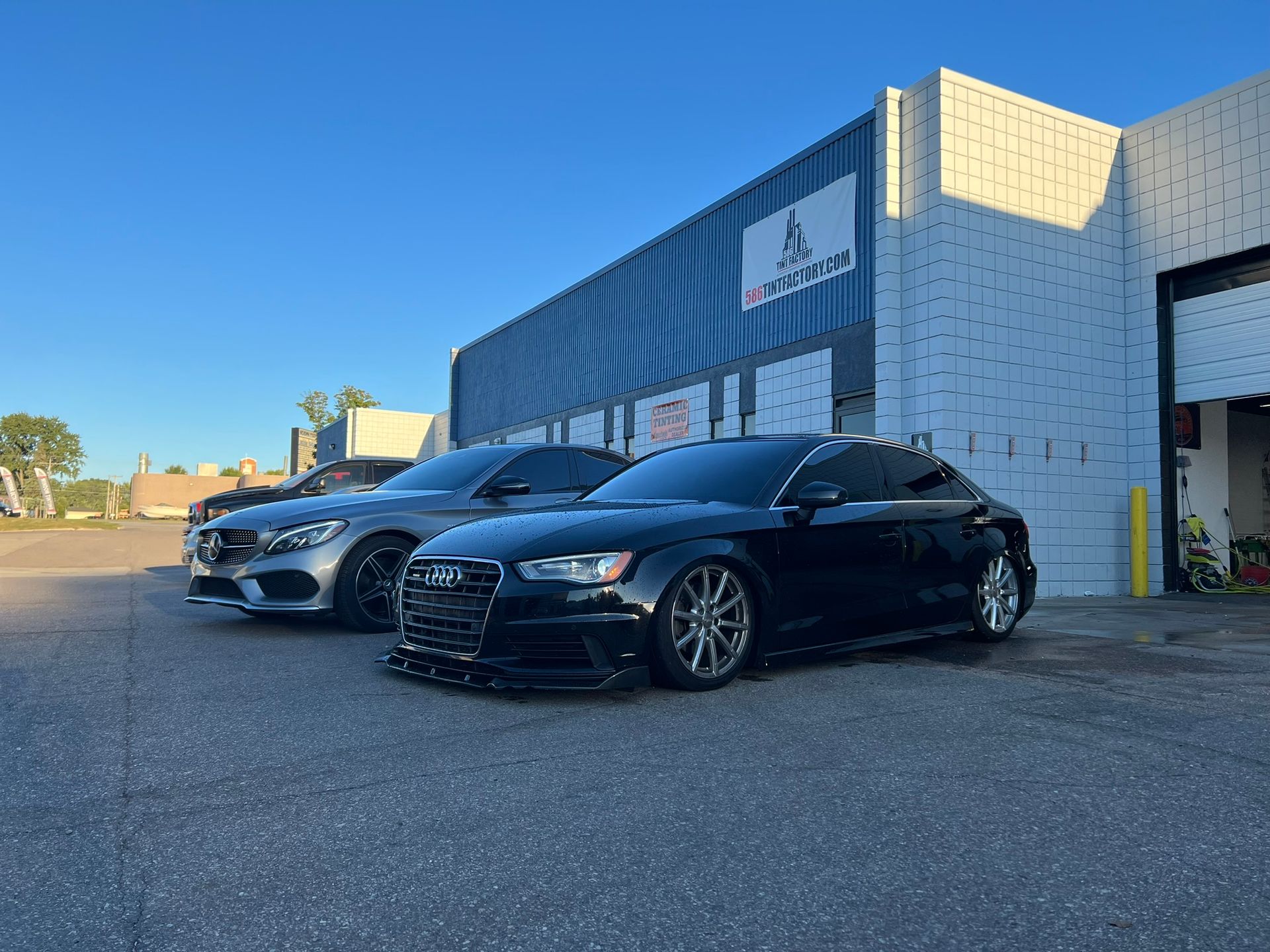 Two parked cars, a black sedan in front of a white building under a clear blue sky.