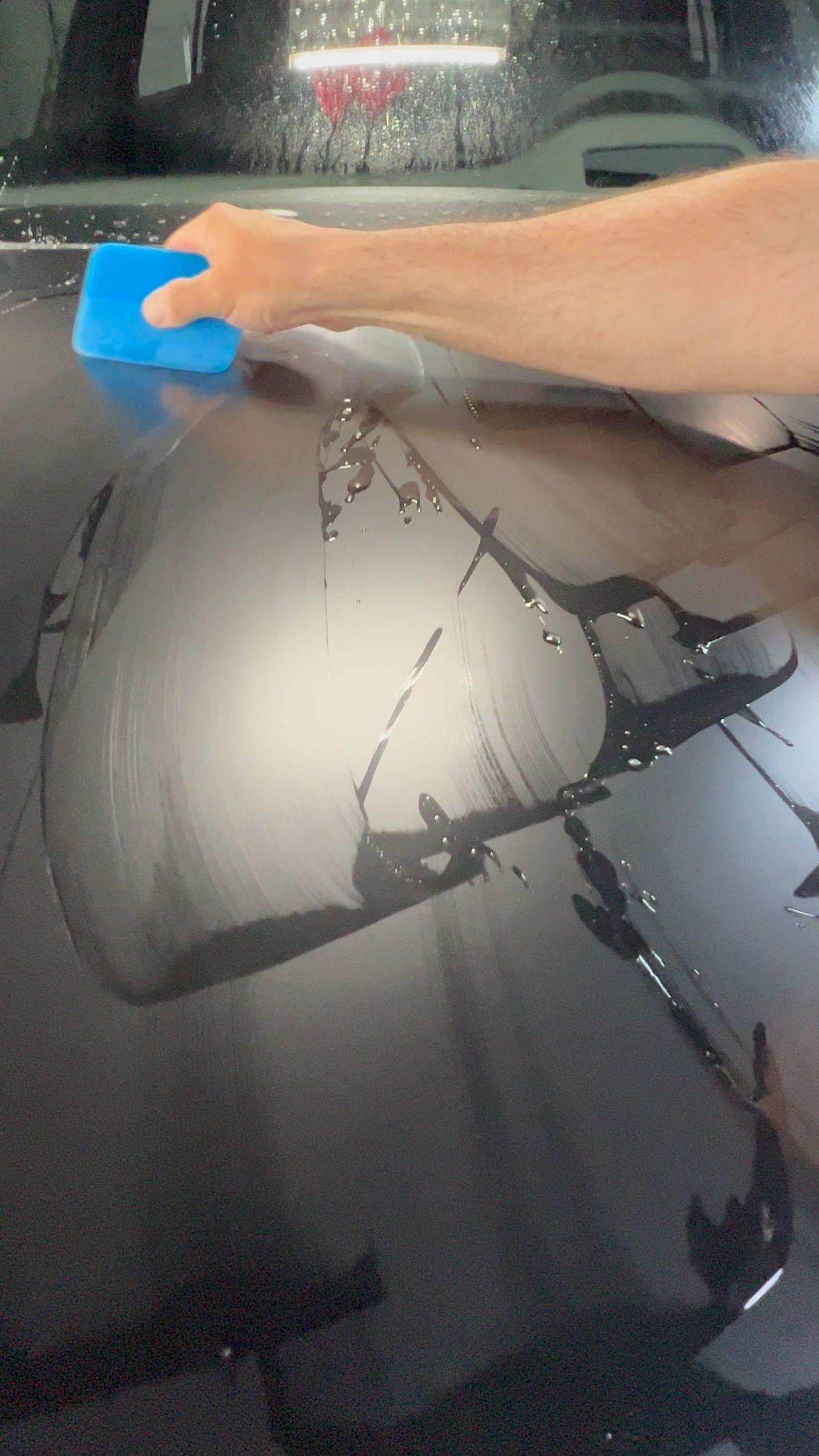 Hand using a blue squeegee to clear water from a fogged car windshield