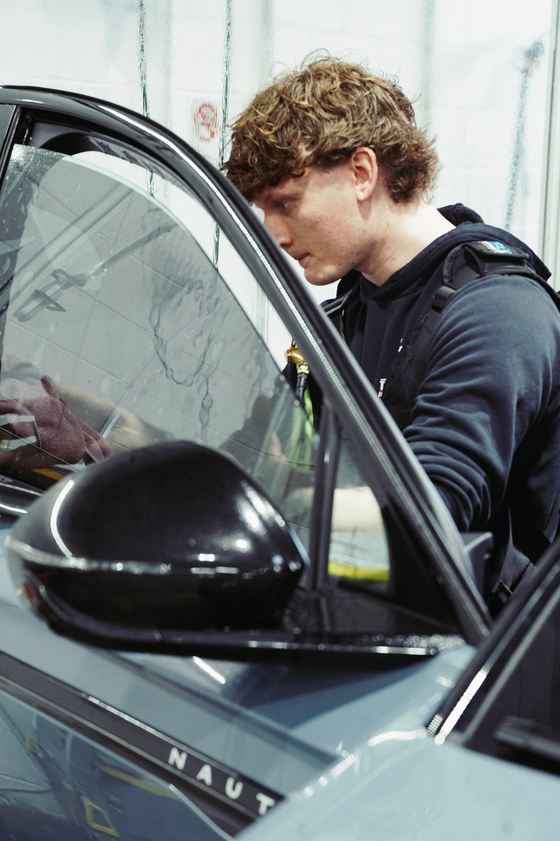 Person standing beside an open car door, leaning into the vehicle in a dark jacket.