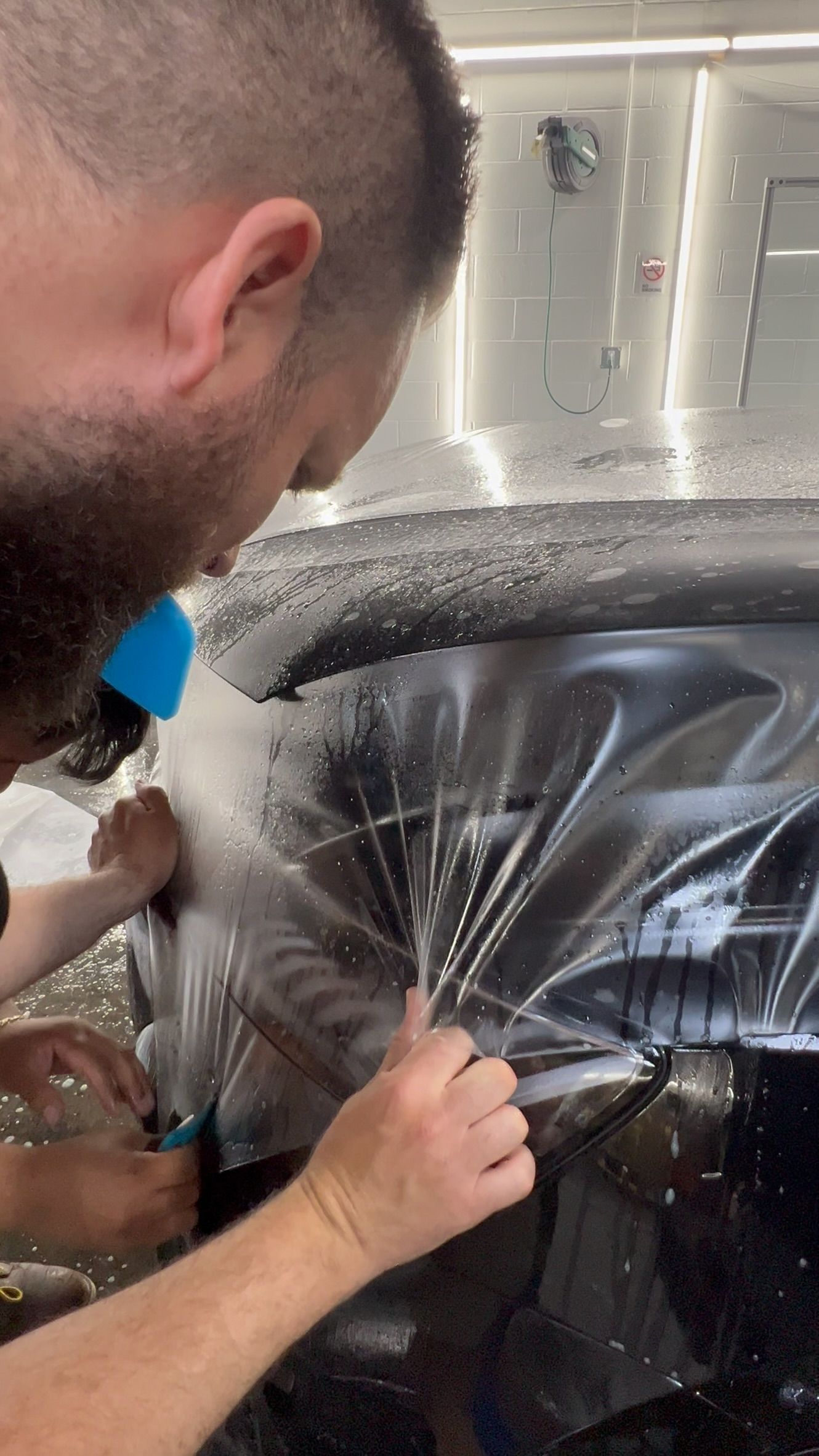 Technician spraying water onto a car window during auto detailing