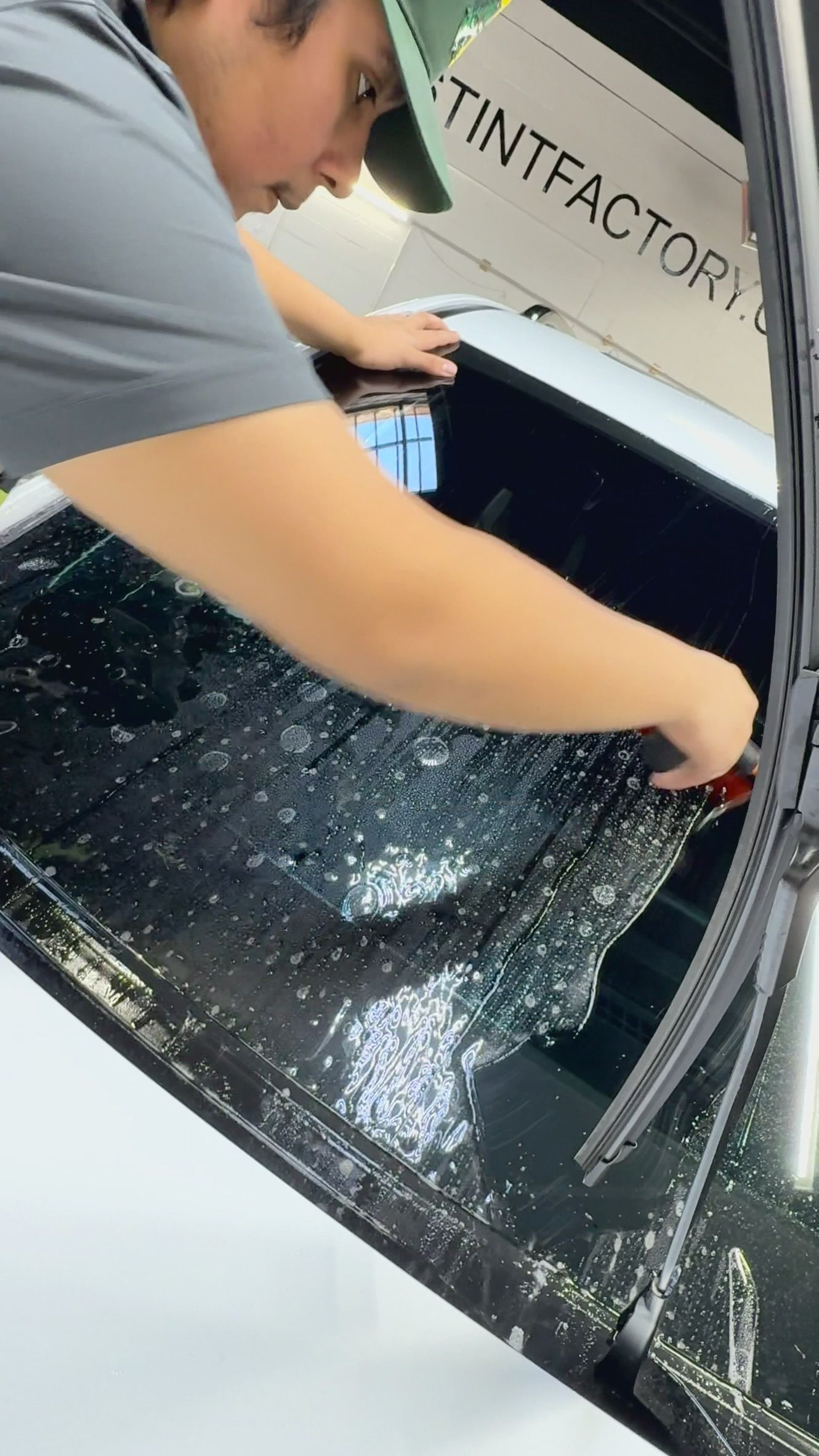Person loading shattered glass into a car trunk with a shattered rear window