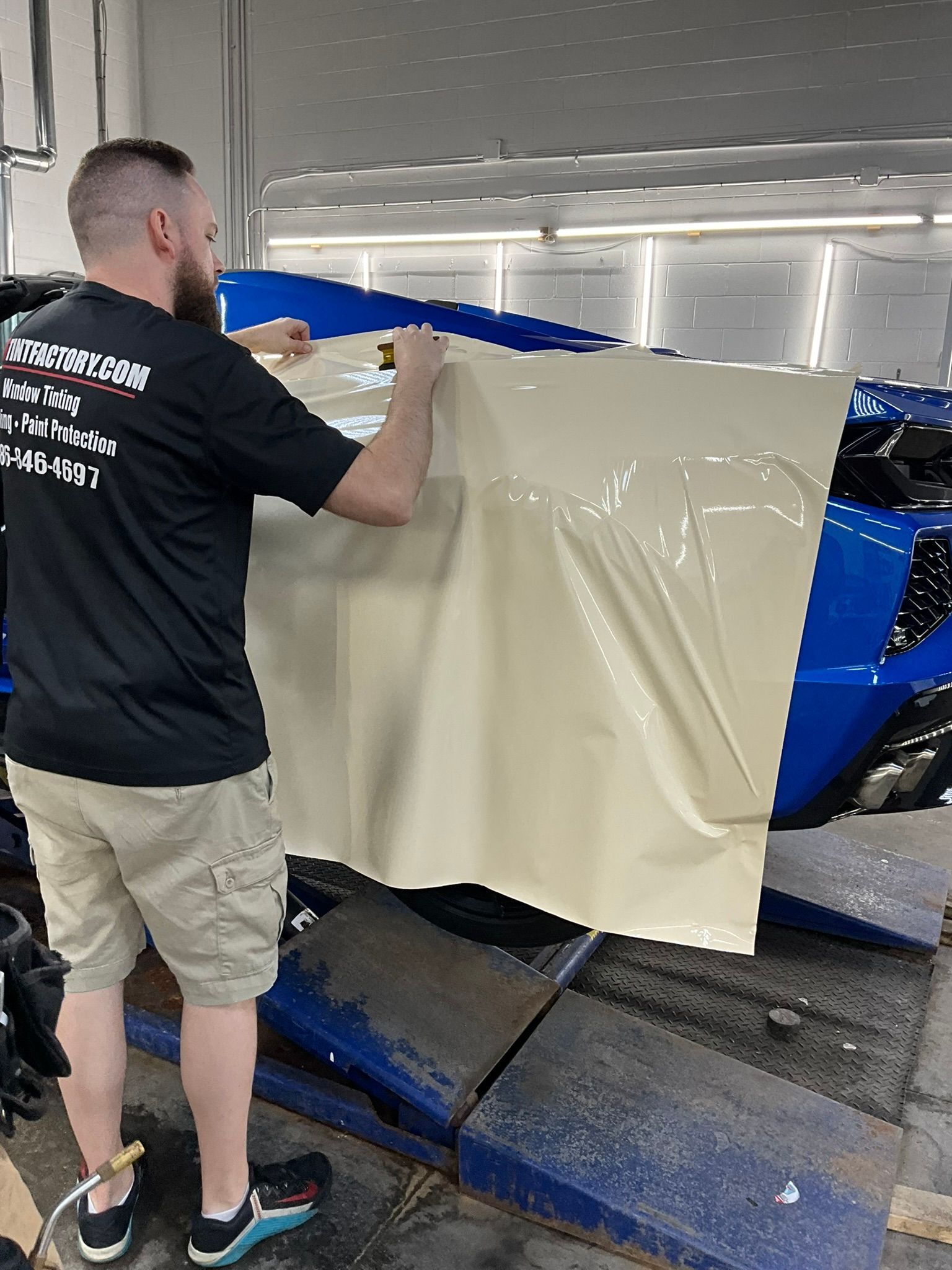 Man covering blue machinery with beige plastic sheeting in a workshop