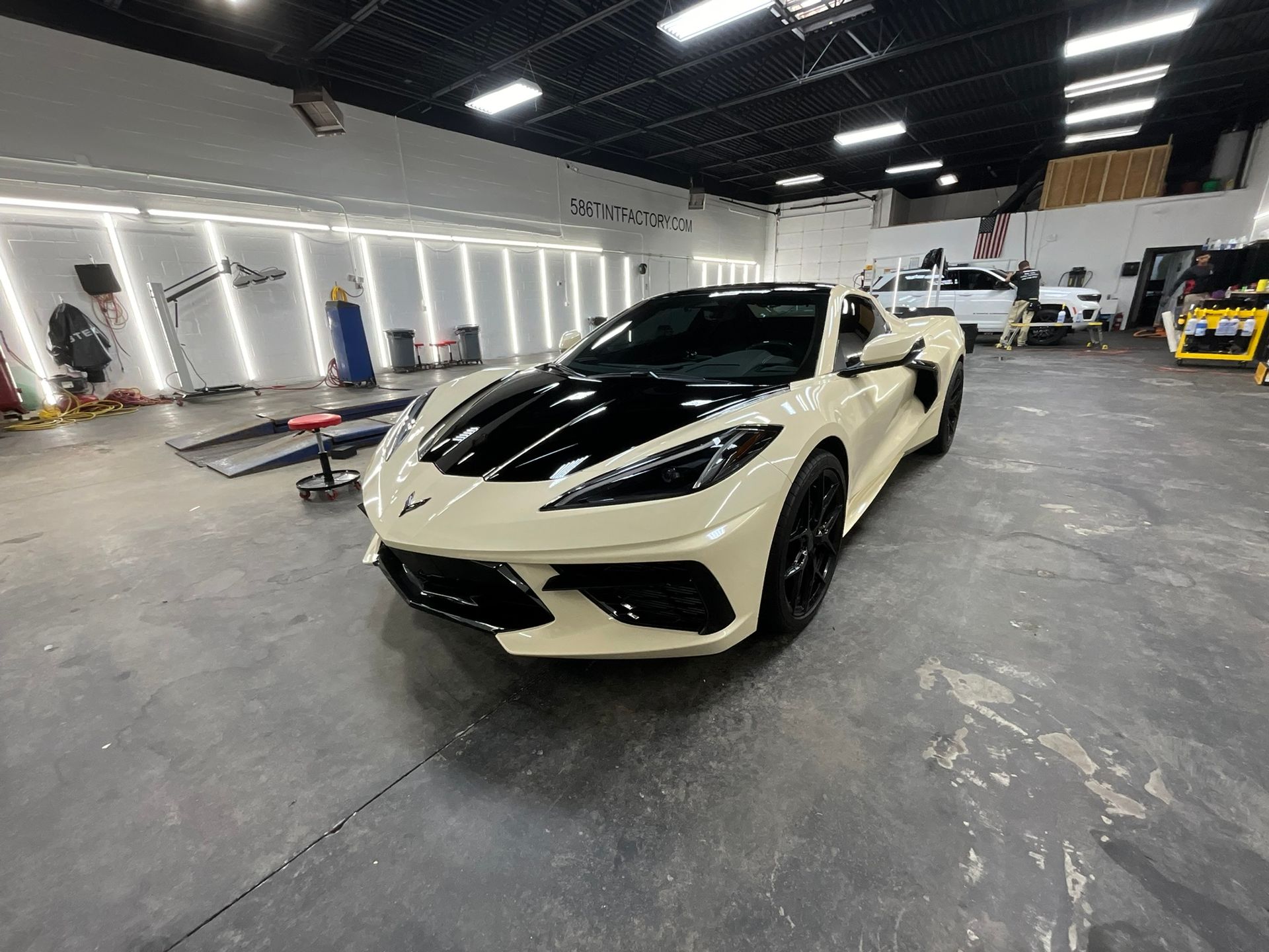 Cream sports car in a workshop garage with bright overhead lights and equipment in the background