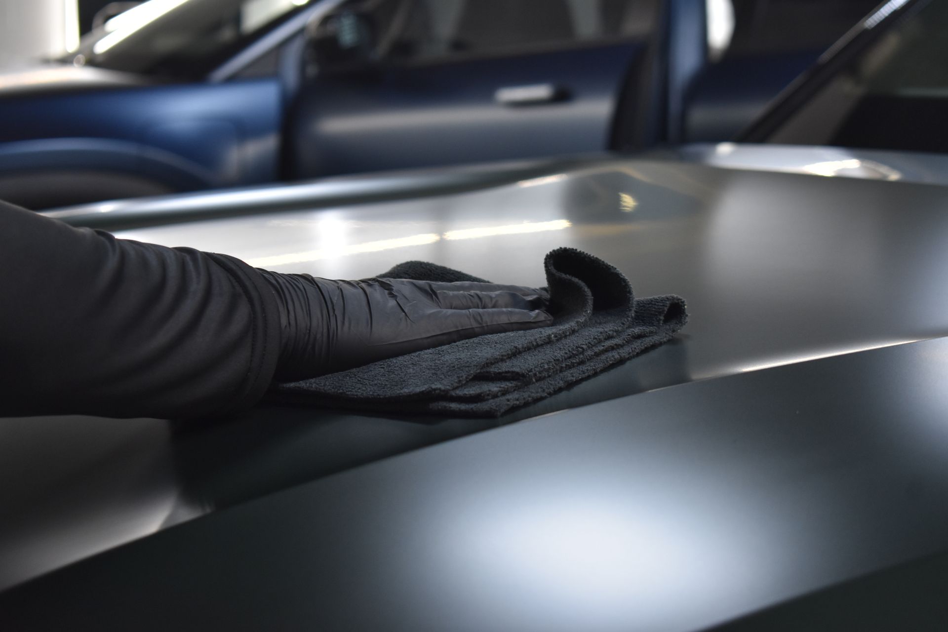 Black-gloved hand wiping a matte gray car hood in a garage