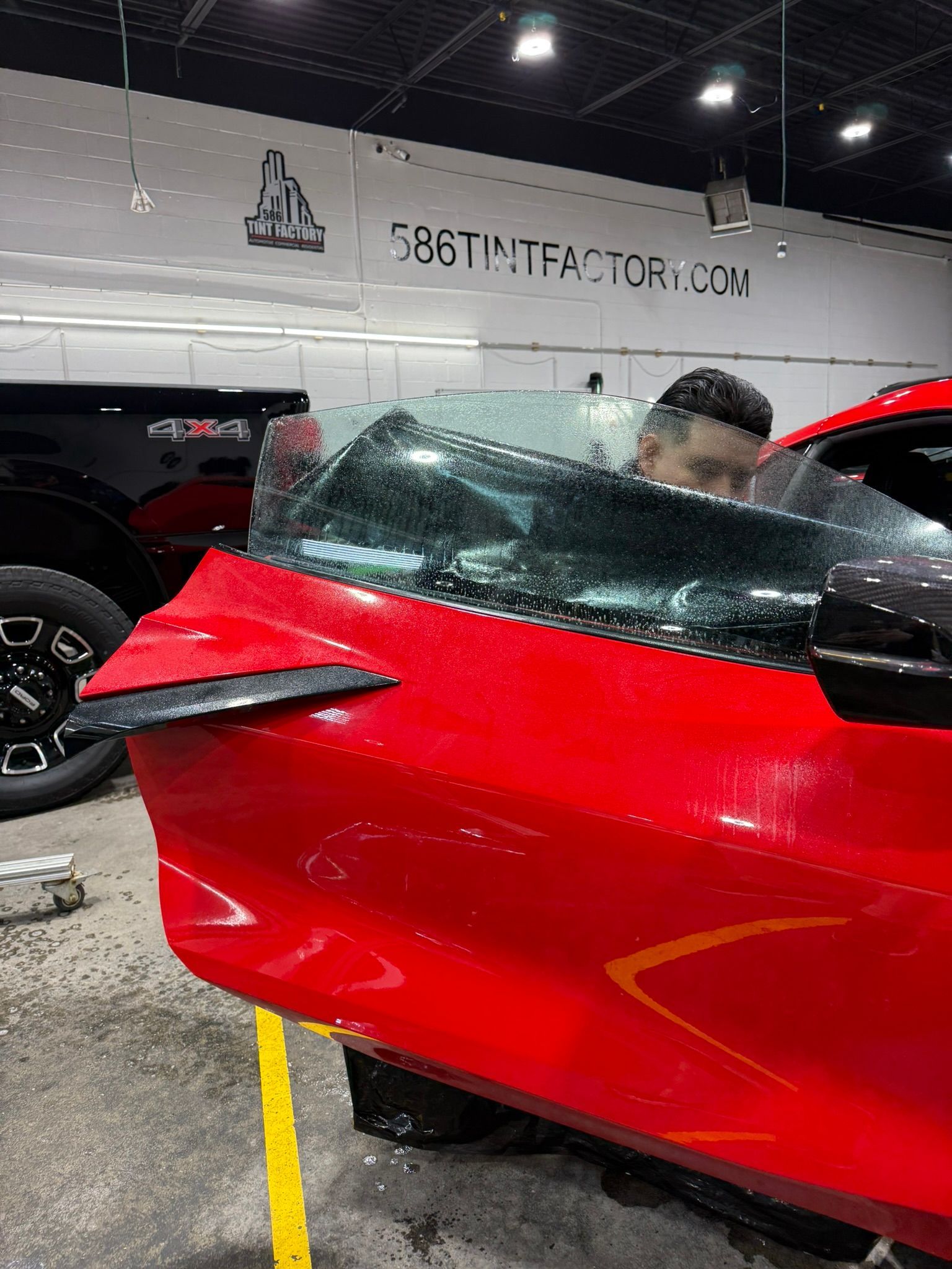 Man applying decals to a red sports car in a workshop