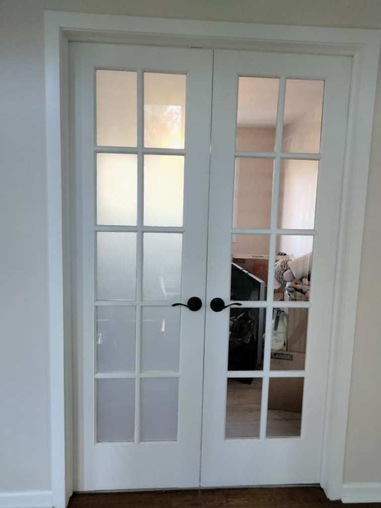 White French doors with frosted glass panels and black knobs in a bright interior hallway