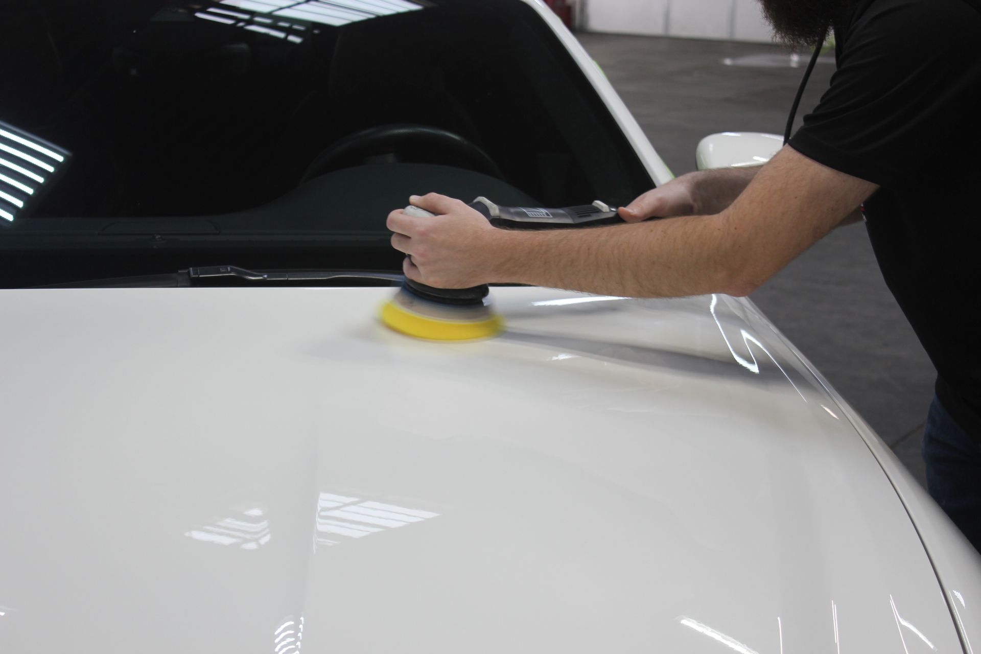 Person polishing a white car hood with a buffer in a garage