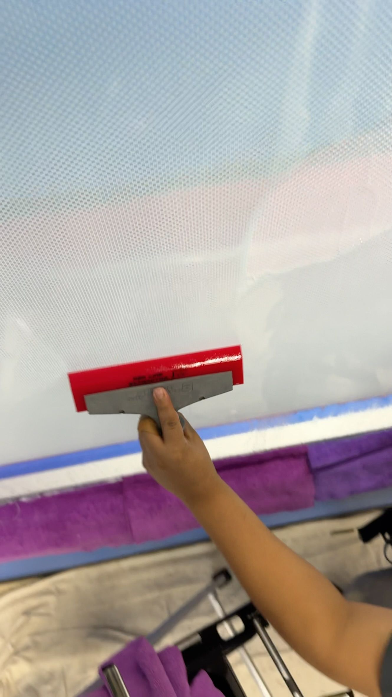 Hand using a red squeegee to smooth a white surface on a window or screen.