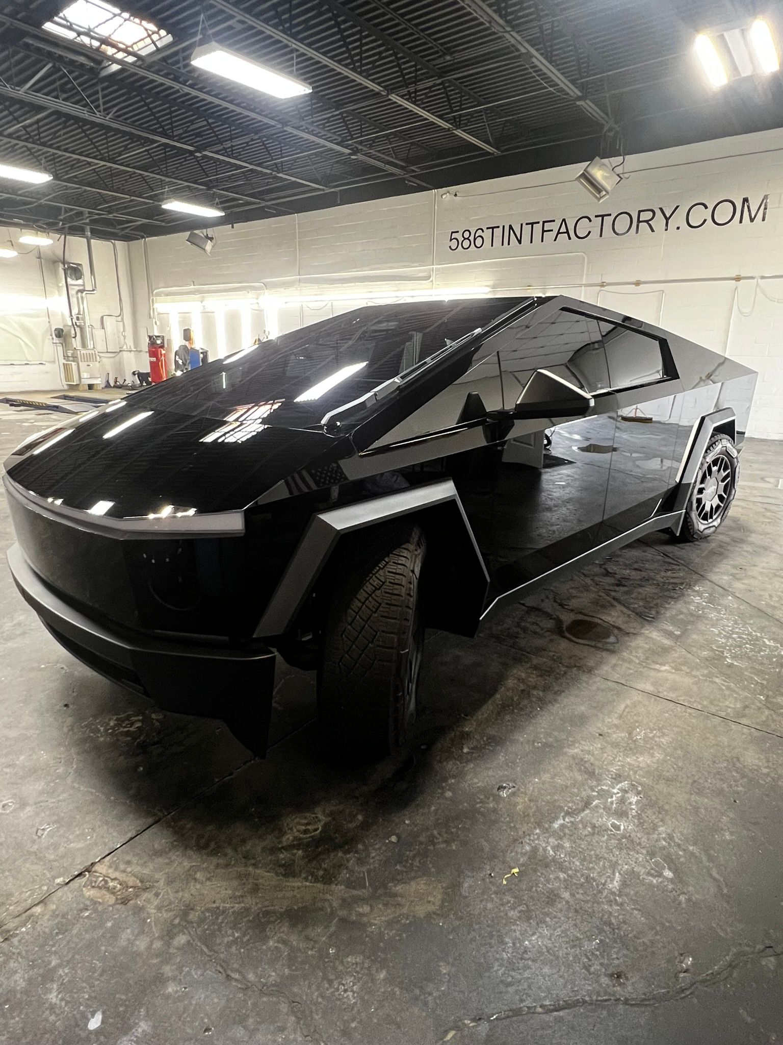 Black Tesla Cybertruck parked indoors in a garage, reflecting overhead lights