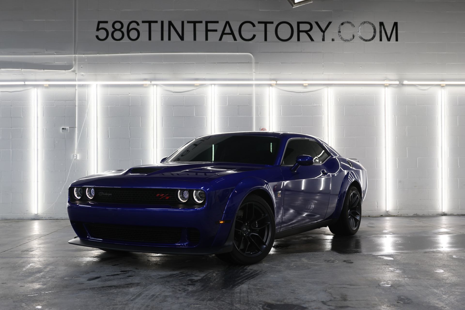 Blue Dodge Challenger in a bright garage, front three-quarter view with wet floor reflections.