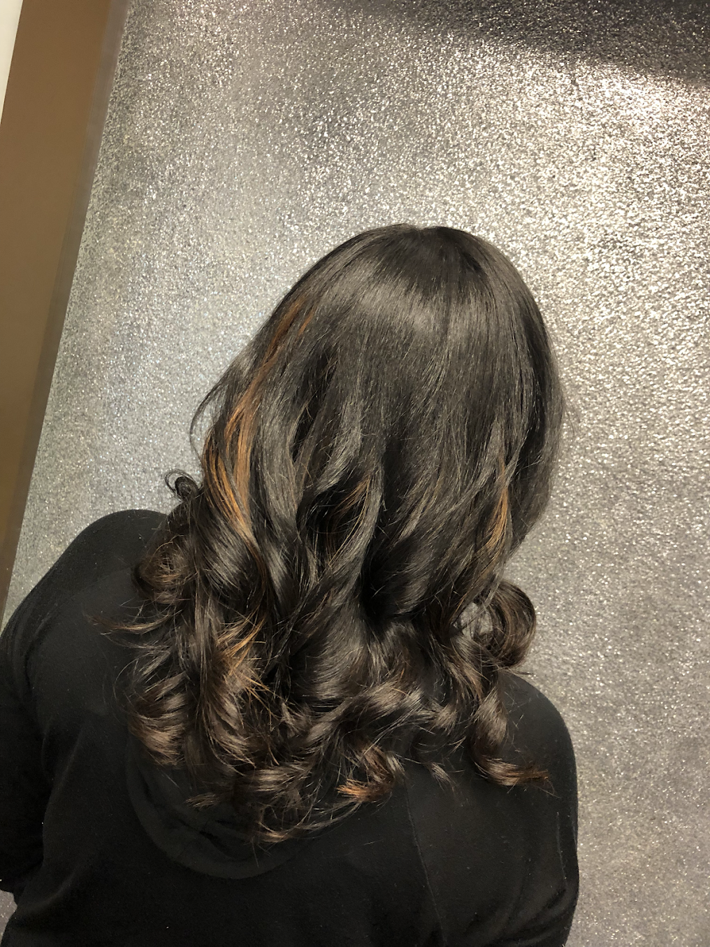 A woman with long black hair is standing in front of a silver wall.