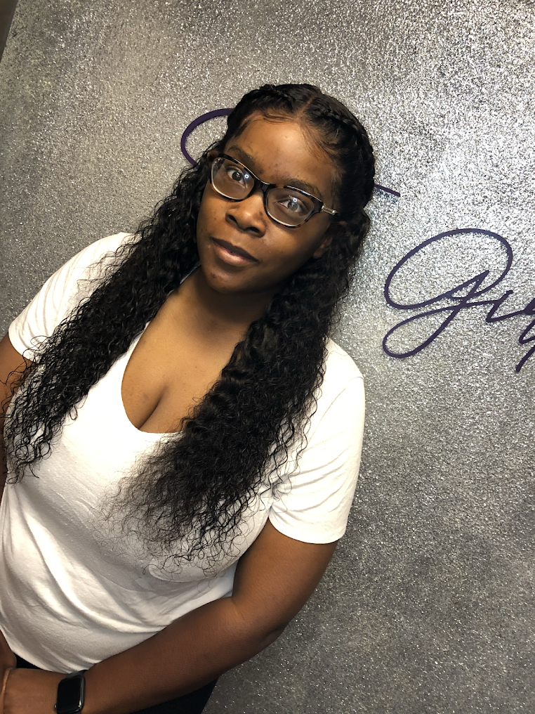 A woman wearing glasses and a white shirt is standing in front of a wall.