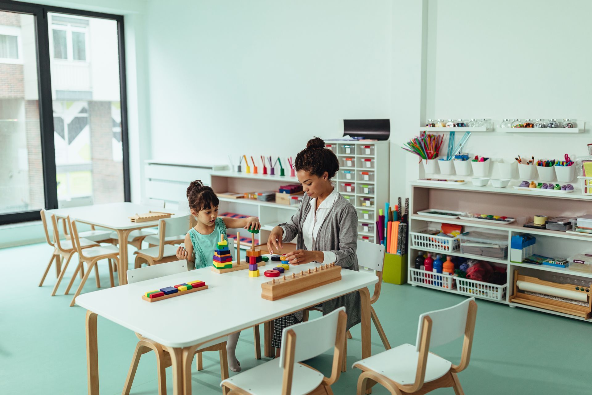 Two children playing with blocks at a white table in a bright classroom