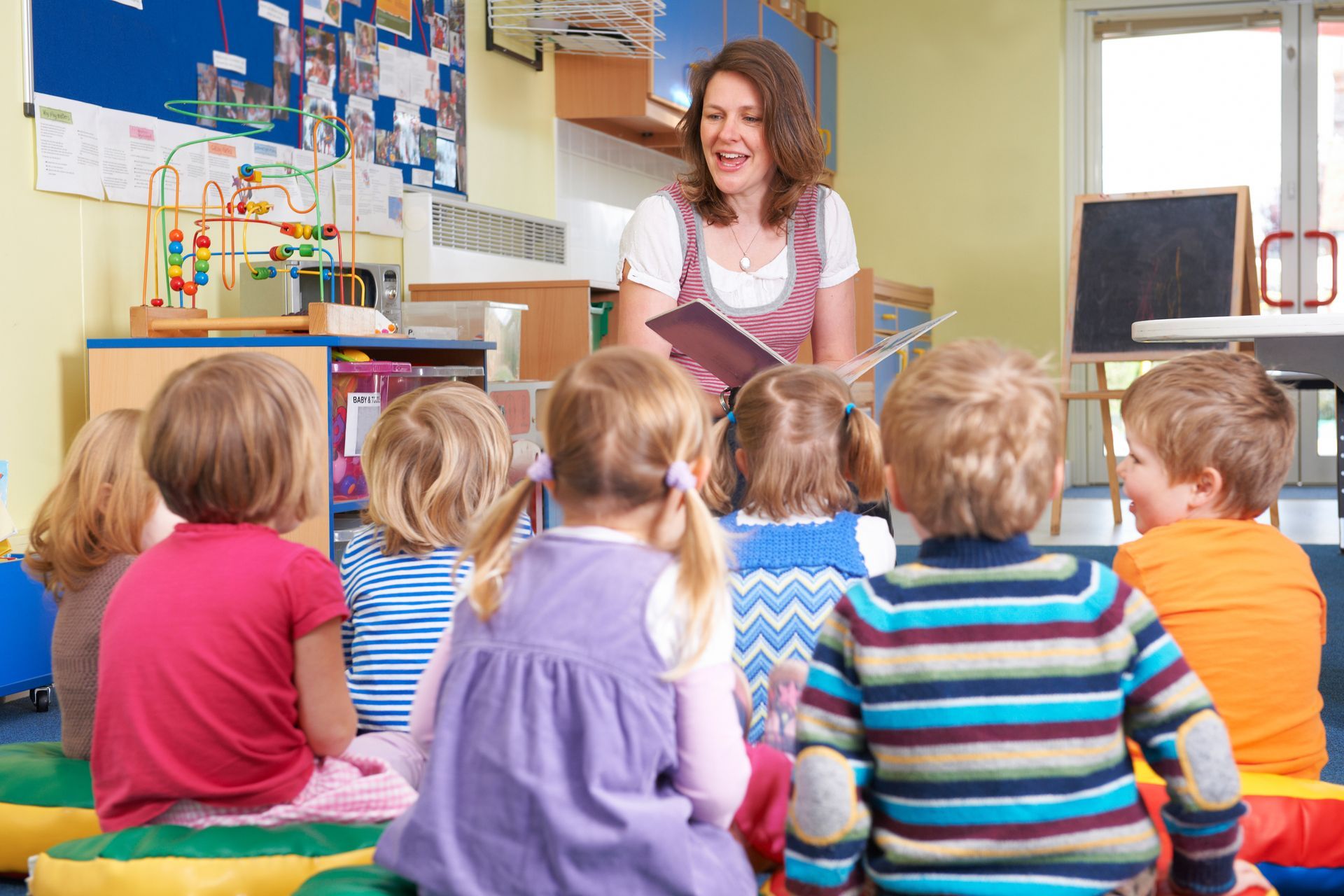 Teacher reading to a seated group of children in a colorful classroom.