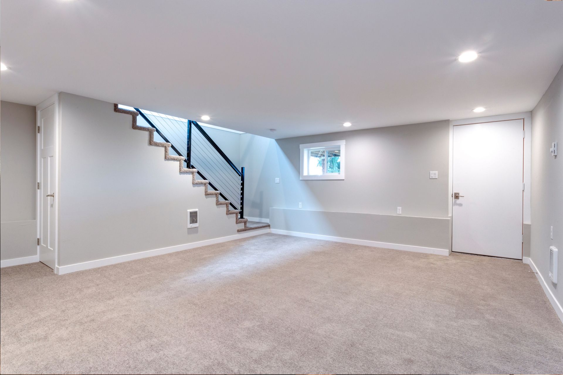An empty basement with a staircase and a window.