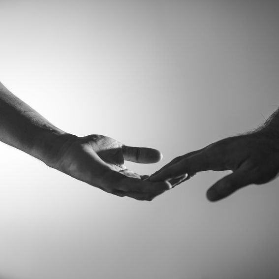 Two hands, in grayscale, reaching toward each other, almost touching fingertips.