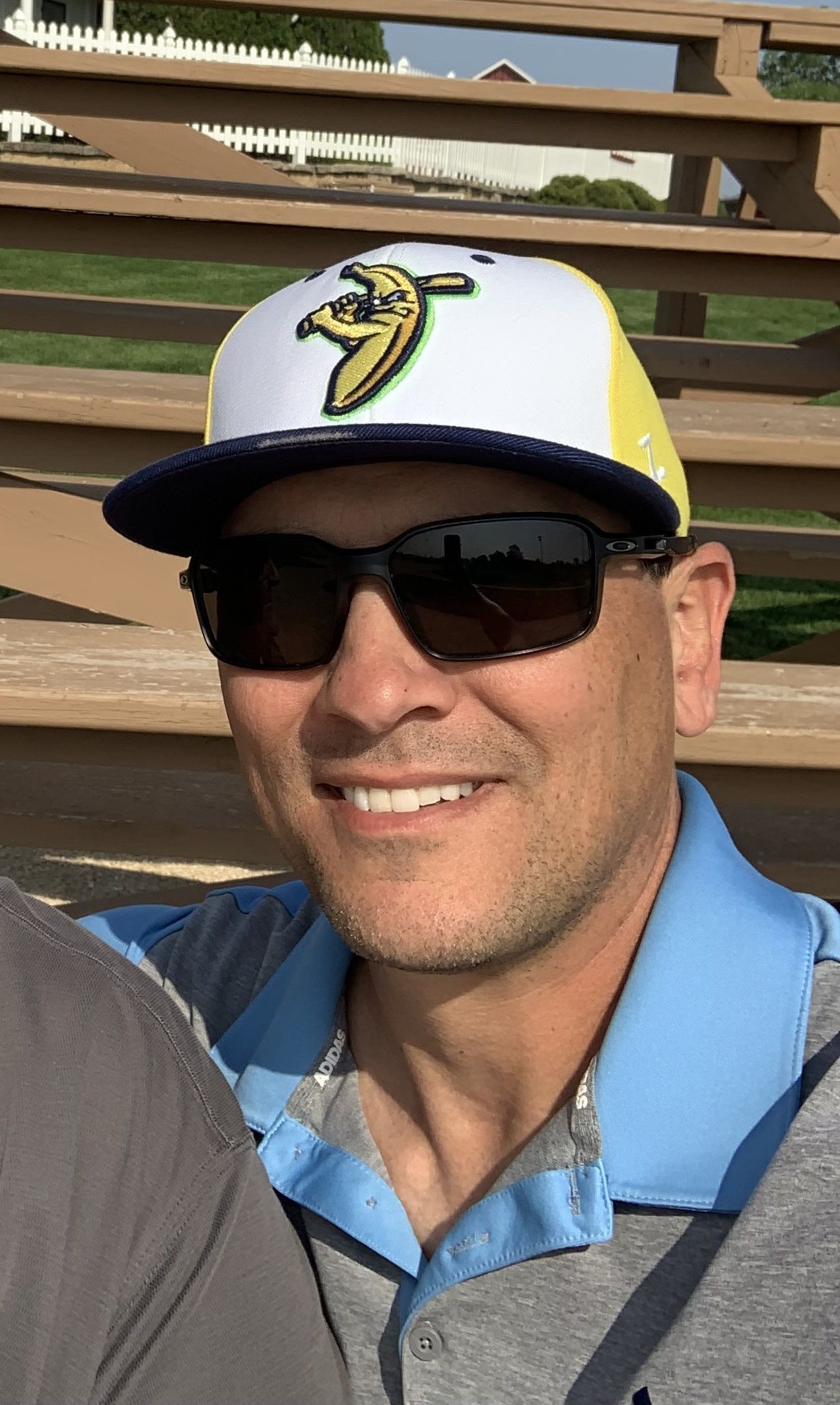 Football coach with arms crossed, standing on a football field. He wears a navy polo shirt and gray pants.