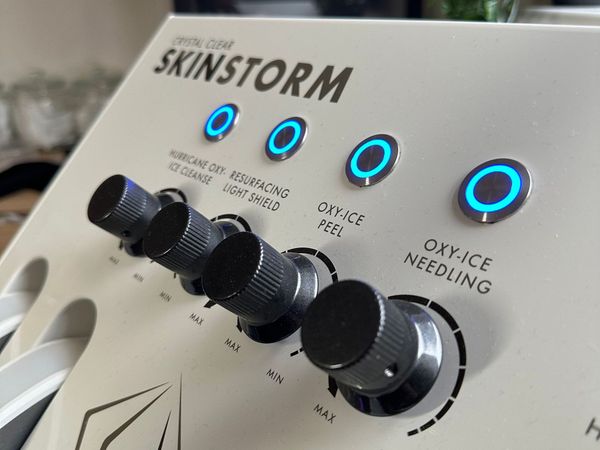 Close-up of a SKINSTORM control panel with four lit blue-ringed knobs and labeled settings.