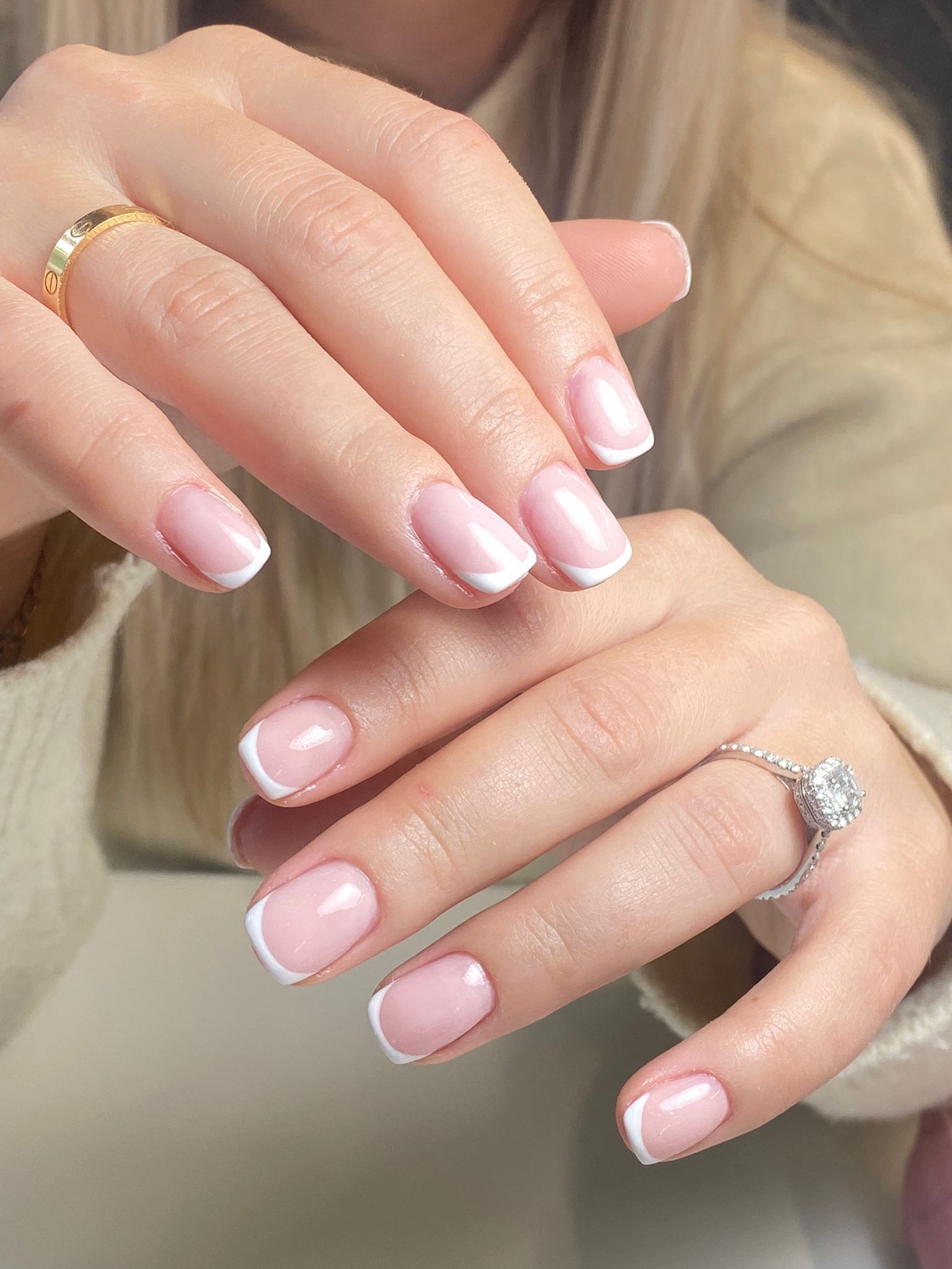 Hands with pale pink French manicure and a silver ring, resting together on a light background