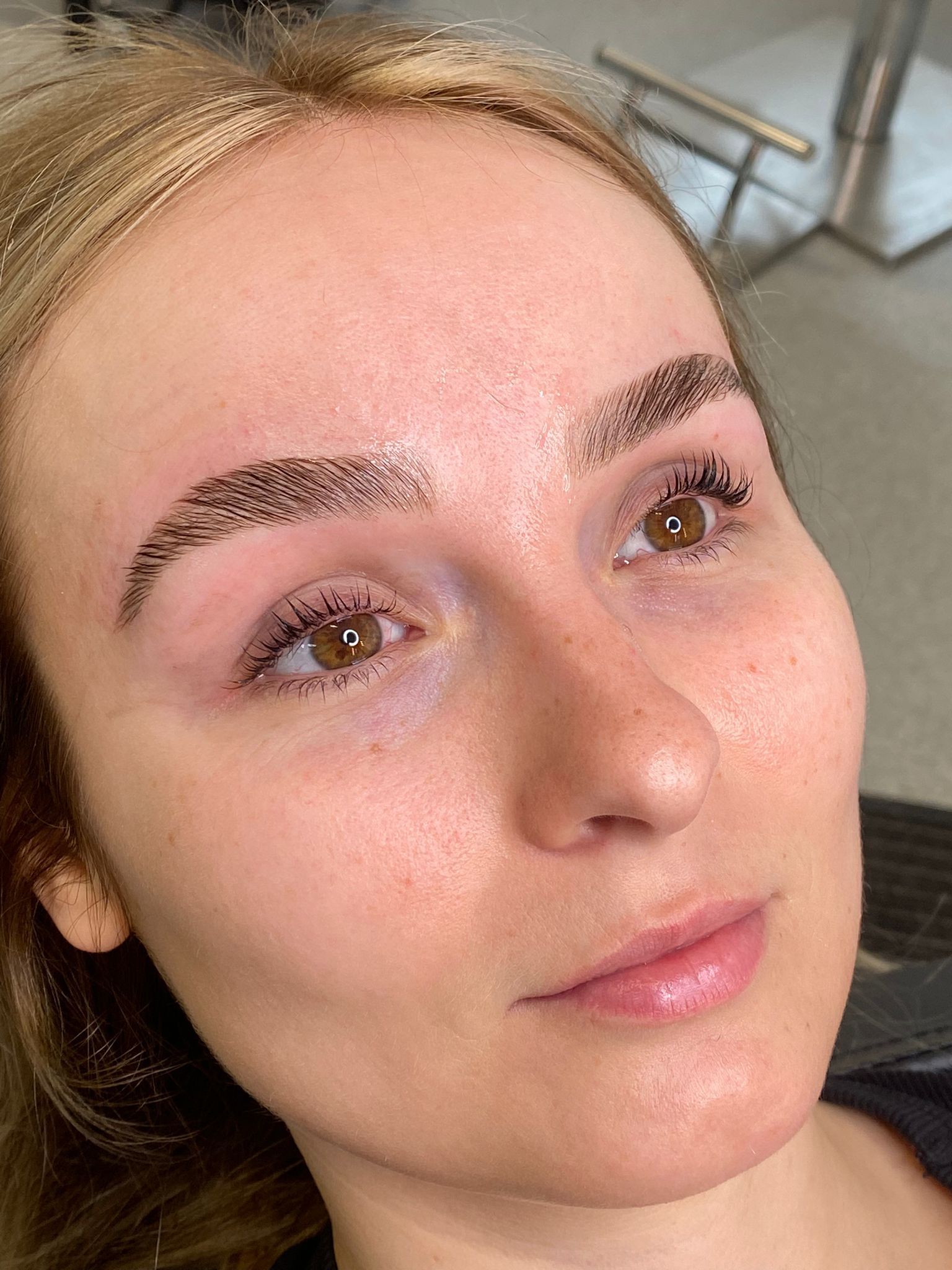 Close-up of a person with natural brows and glossy lips, lying down and looking upward indoors