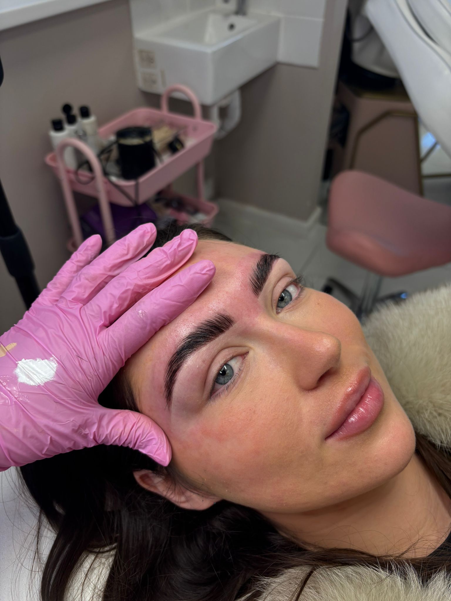 Woman lying on a treatment bed while a gloved hand touches her forehead in a spa or clinic setting