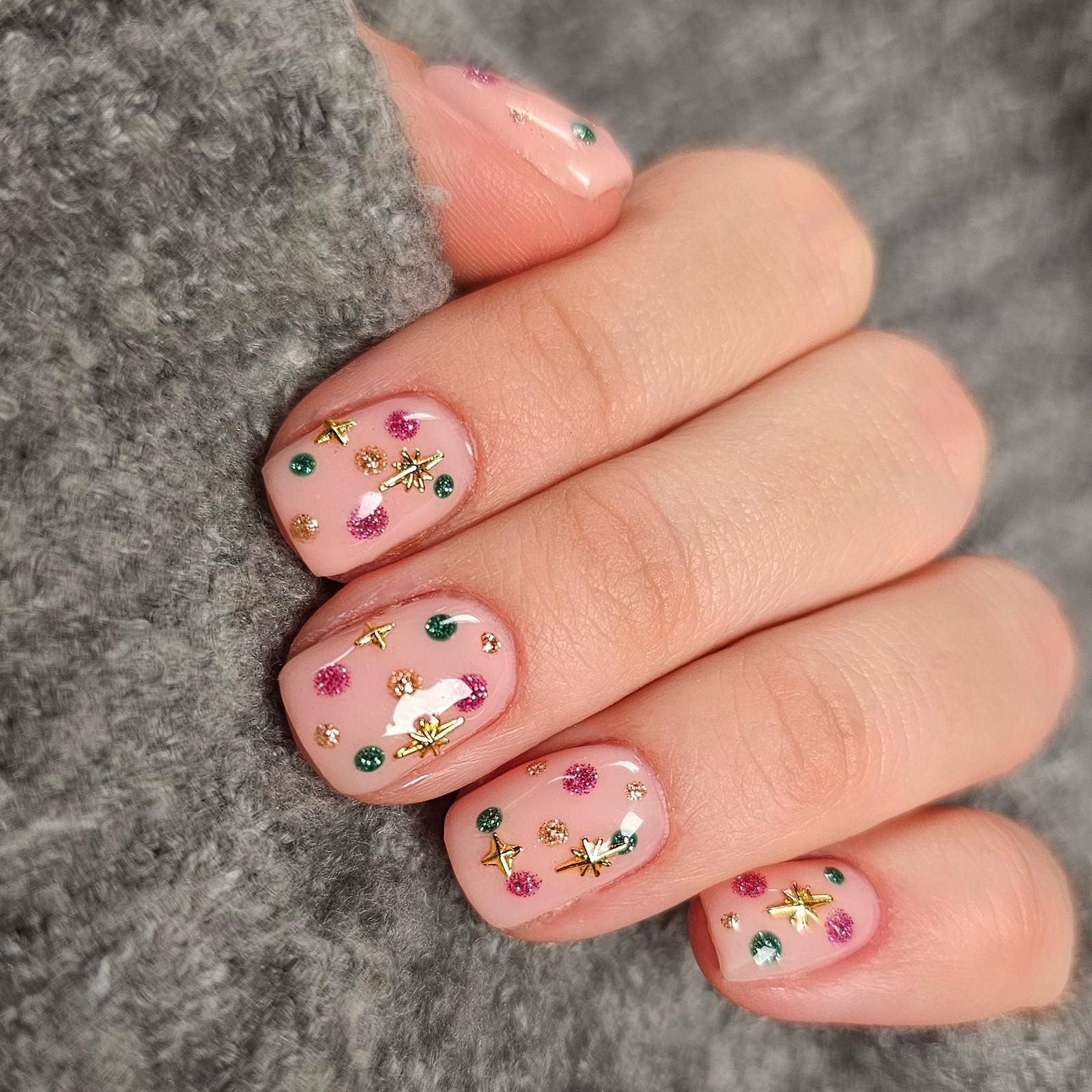 Hand with pink nails decorated with colorful star and gem nail art, resting on gray fabric.