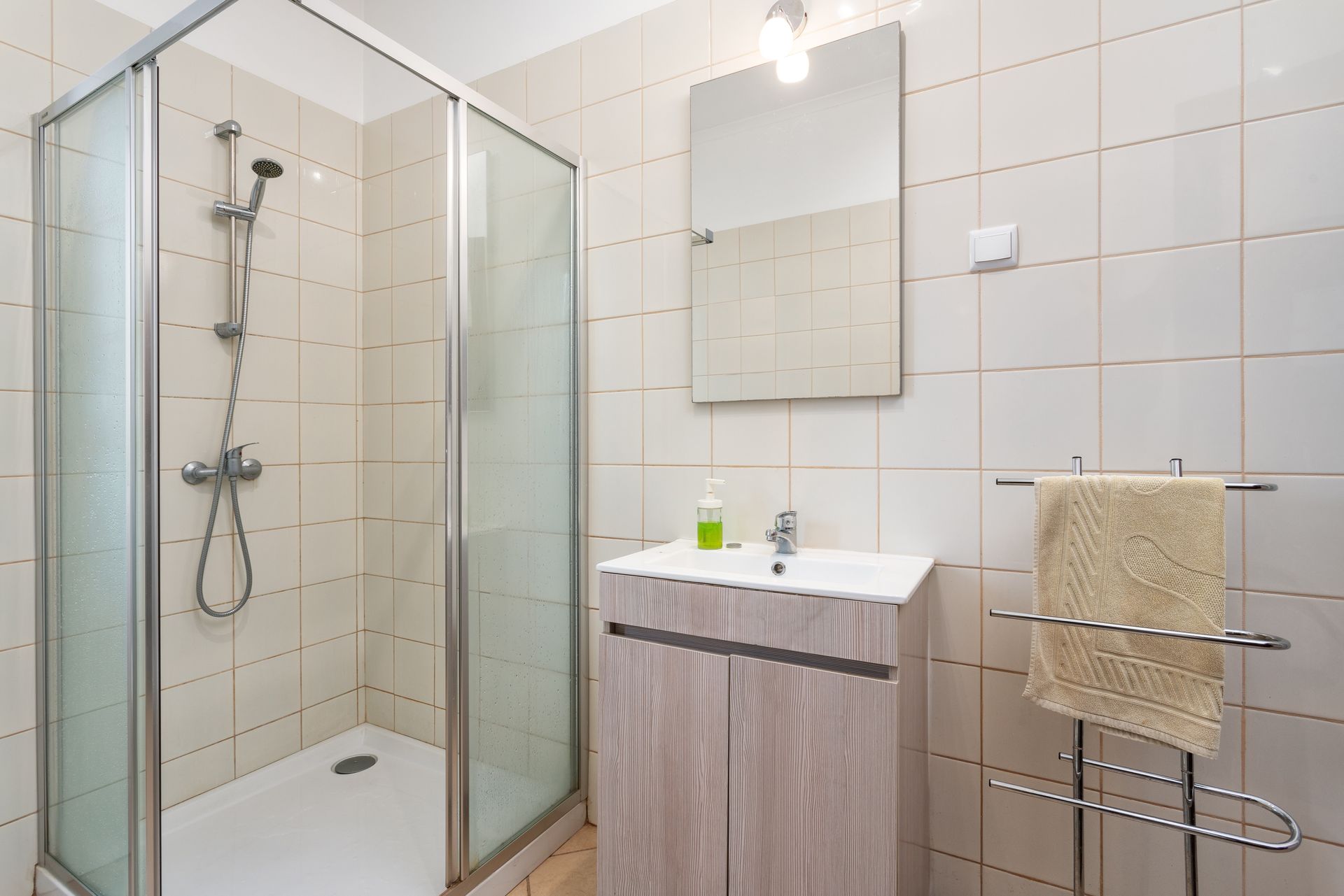 Modern bathroom with glass shower, vanity sink, mirror, and towel rack against white tiled walls