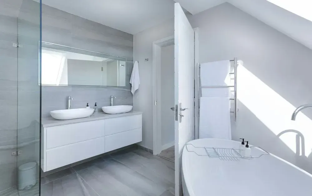 Bright modern bathroom with glass shower, double vanity, and a freestanding tub by a window.
