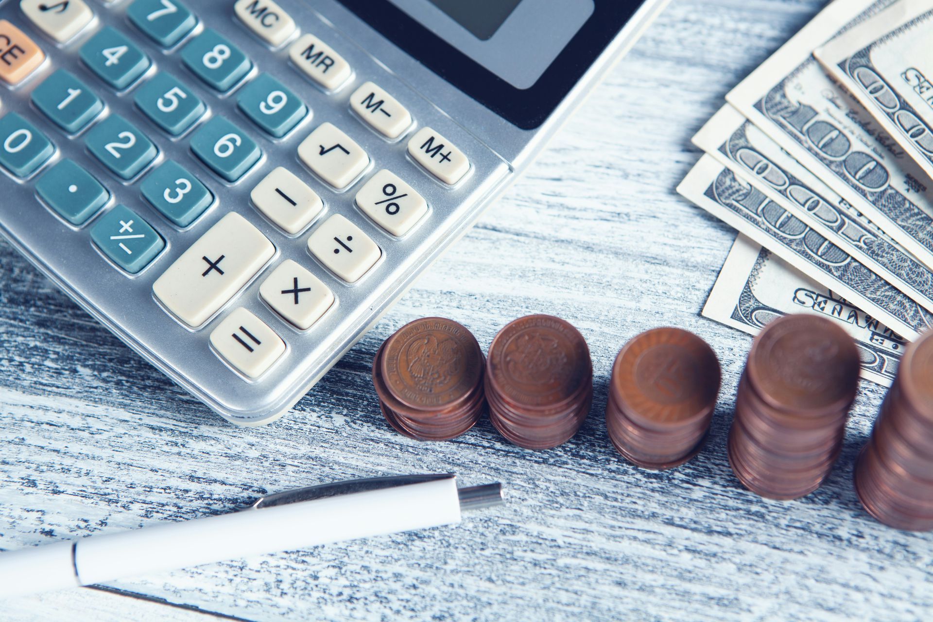 Calculator with stacked coins and a pen on a wooden desk, suggesting budgeting or financial planning