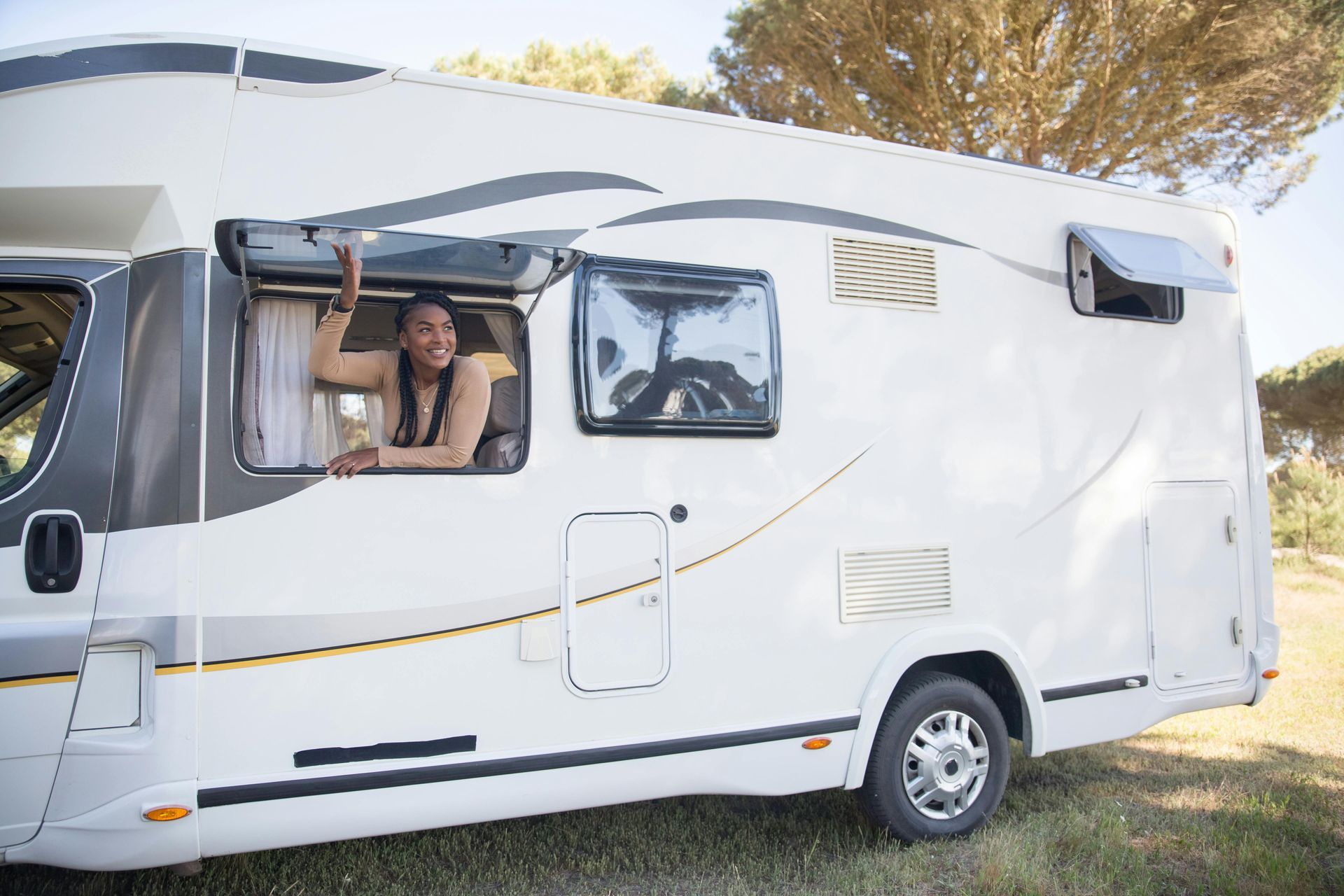 A rv is parked in a grassy area with the sun shining through the trees.