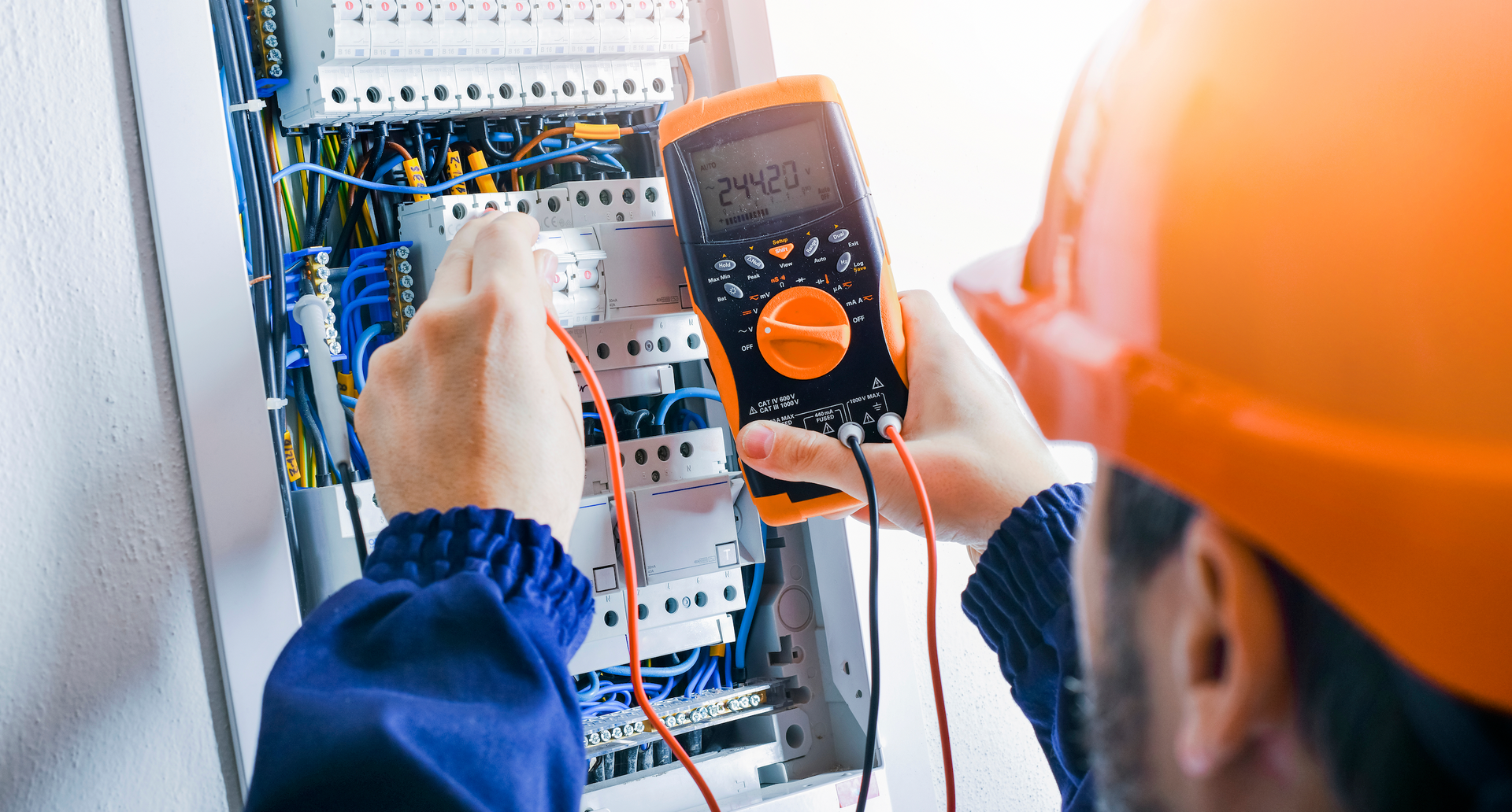 An electrician is using a multimeter to test an electrical box.