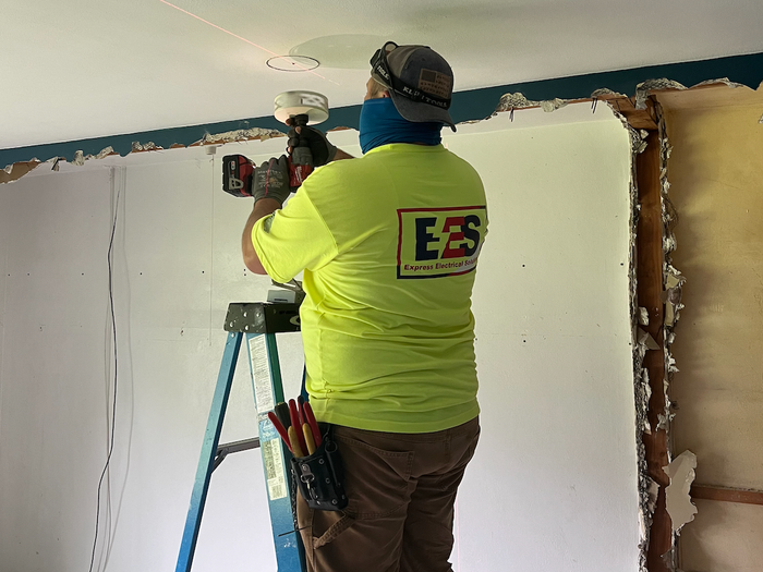 A man is standing on a ladder working on a ceiling.