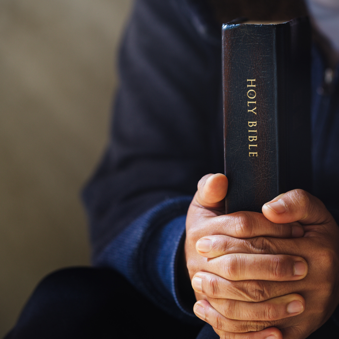 Person holding a black Bible close to the chest, hands clasped.