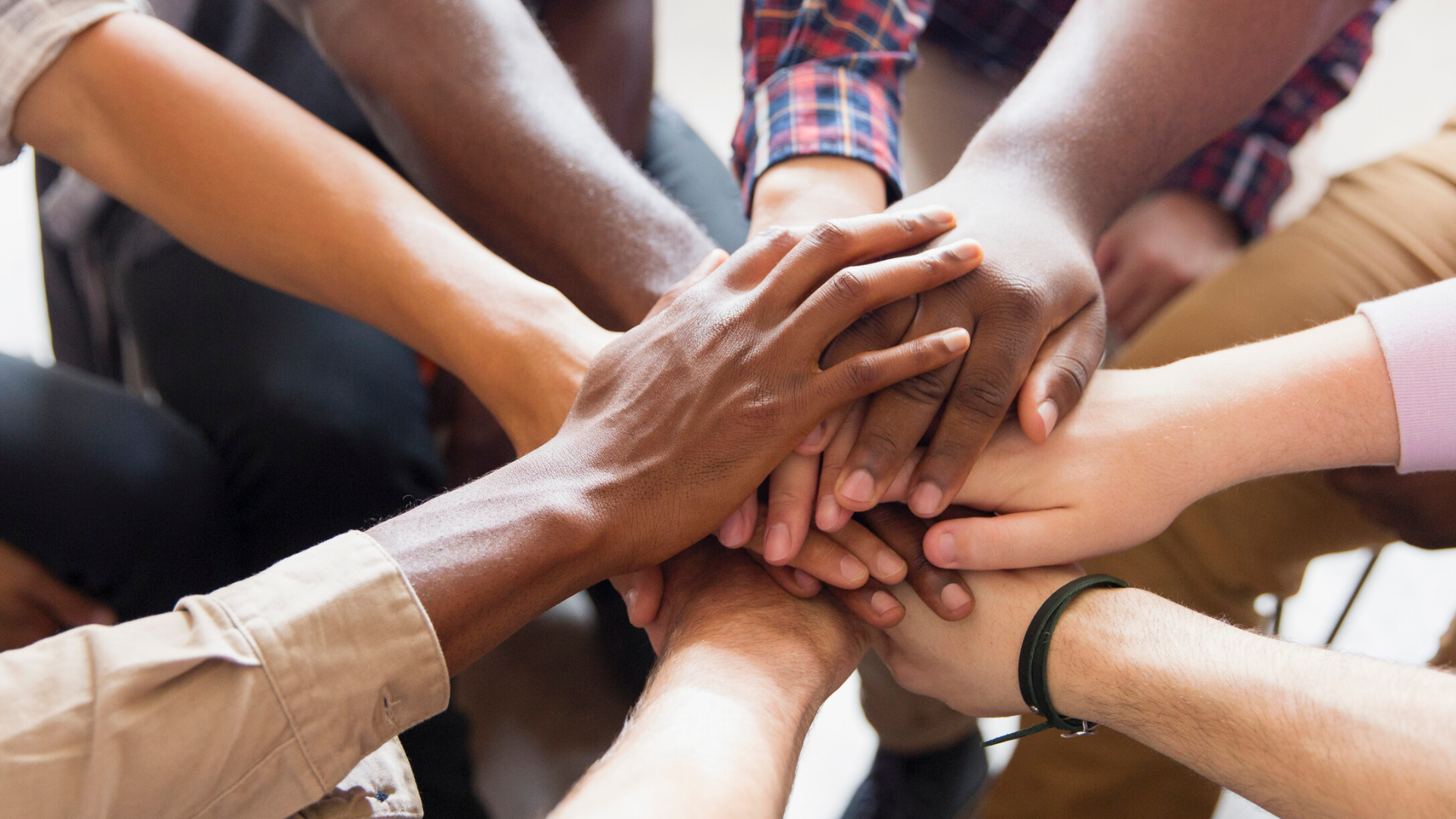 Hands of different skin tones clasped together in a pile, teamwork symbol.