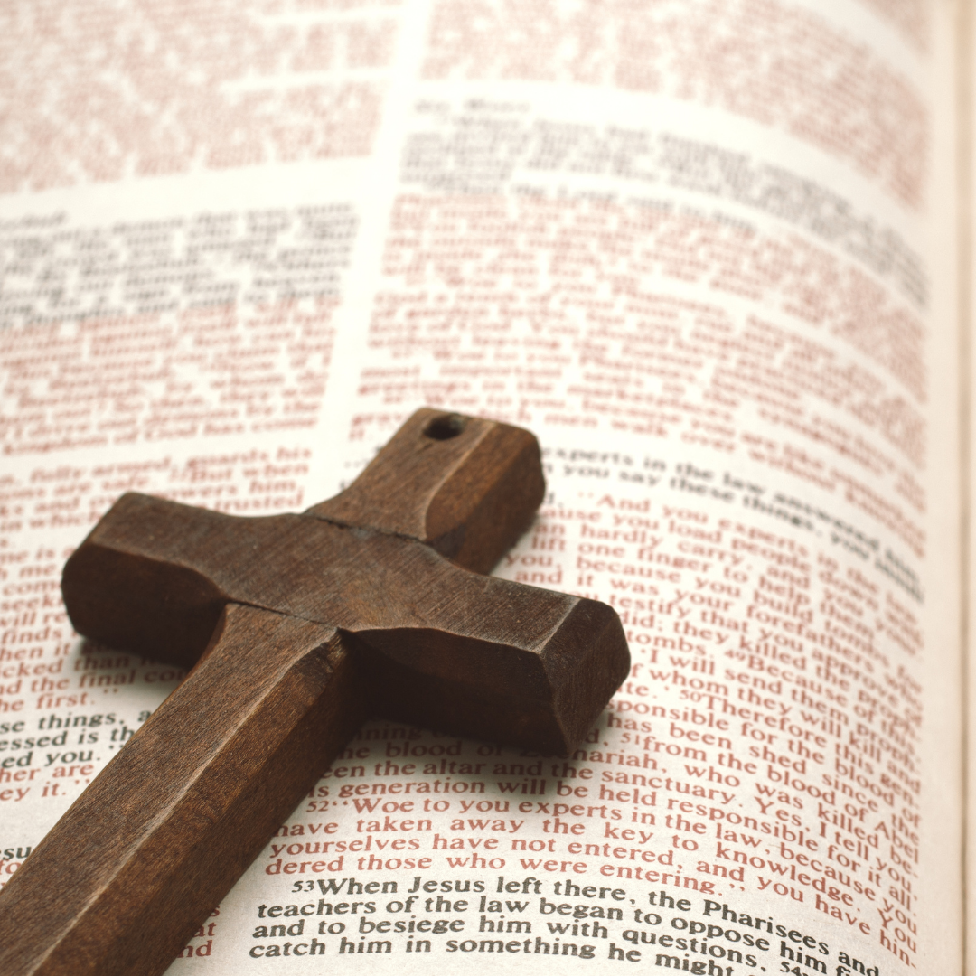 Wooden cross on top of an open book with red text.