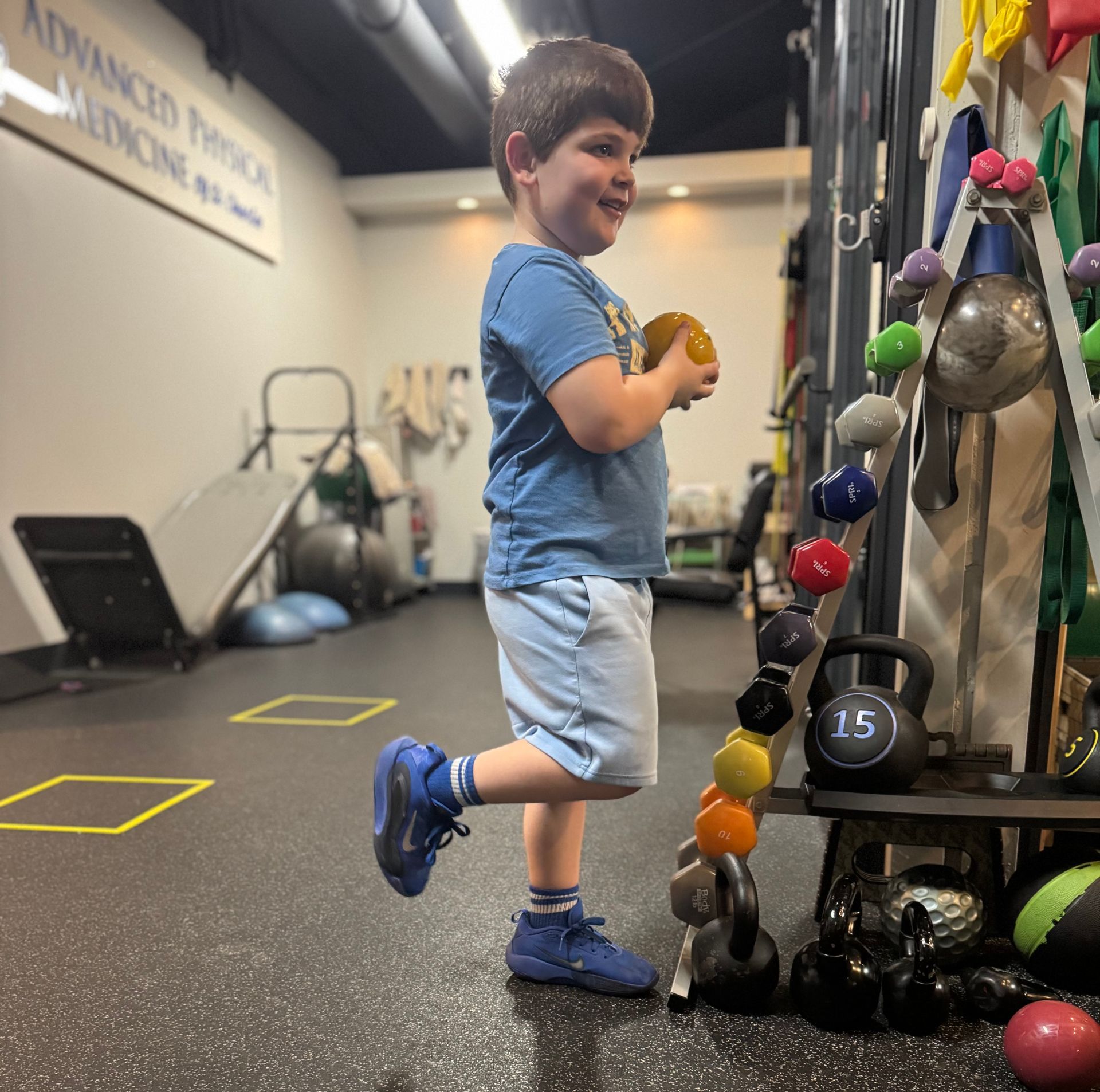 A young boy in a blue shirt is standing next to a kettlebell with the number 25 on it