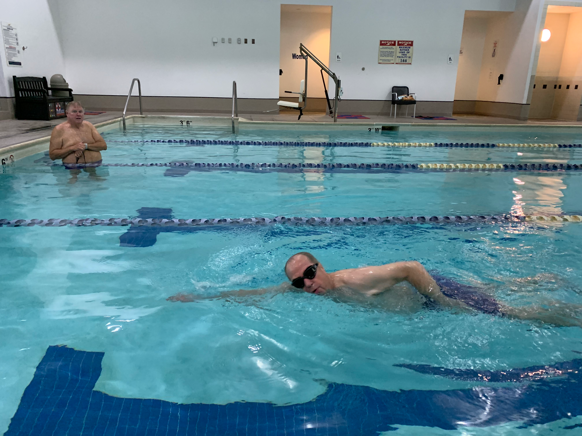 Two men are swimming in a large indoor swimming pool.