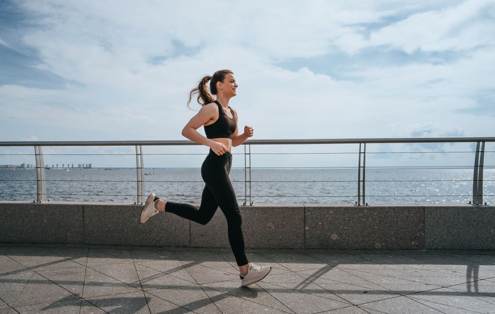Woman jogging along a waterfront promenade under a cloudy sky