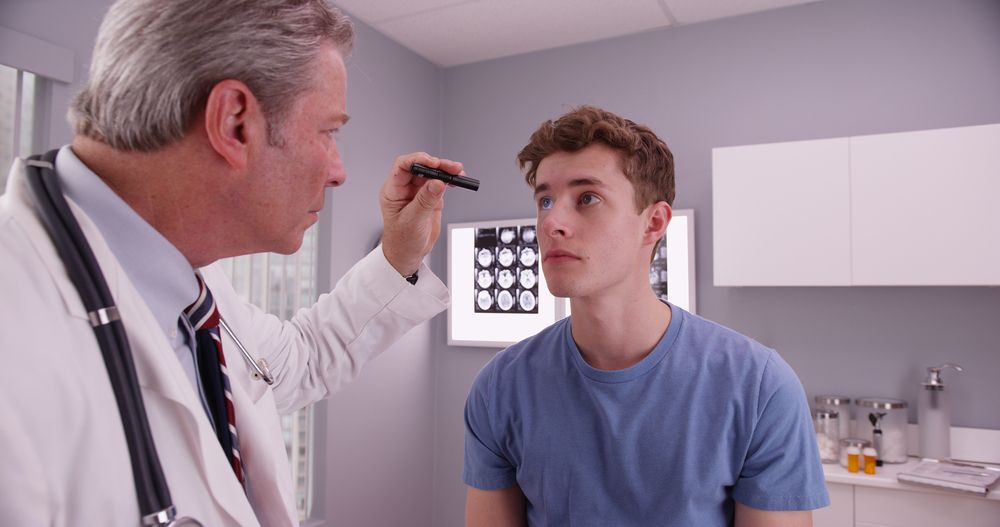 Doctor examining a patient's eye with a light in an office.