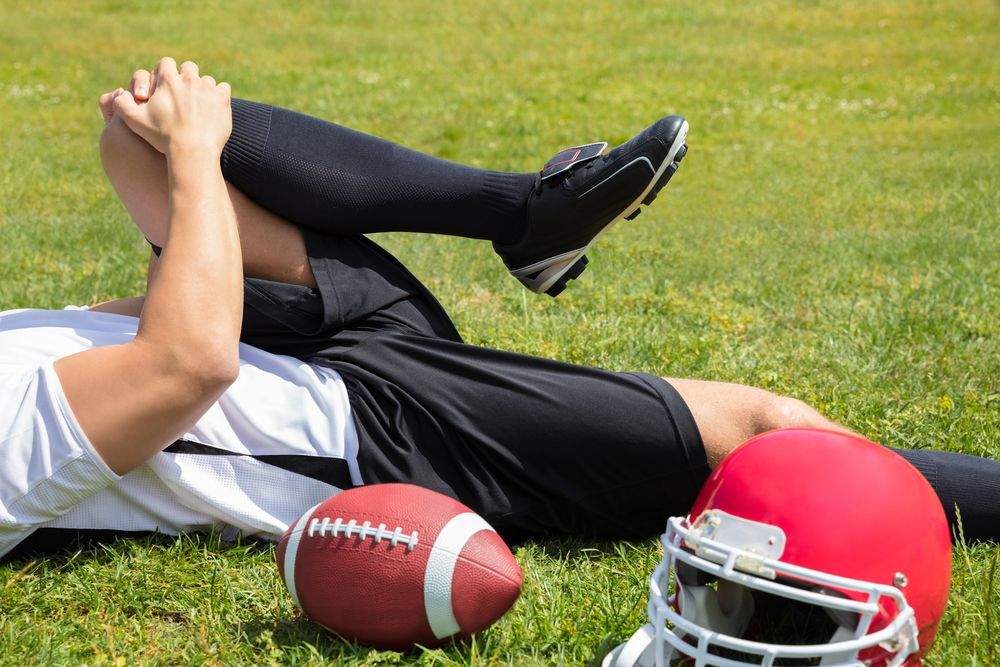 Football player on the grass holding knee, near a helmet and football.