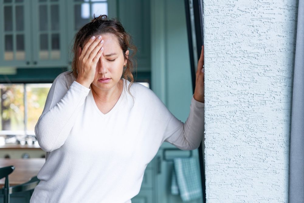 a woman is standing in a kitchen suffering from vertigo.