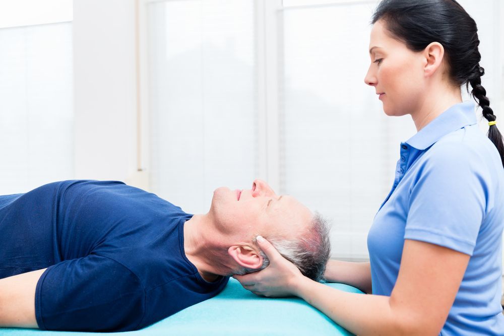 Physical therapist supporting a patient’s head during a neck treatment on a blue table