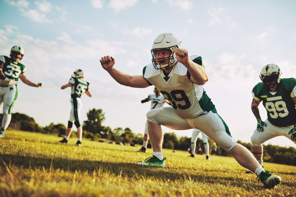Group of young American football players doing drills while practicing outside together on a grassy field in the afternoon.