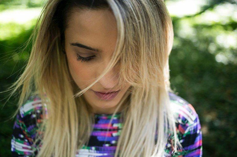 Close-up de uma mulher loira olhando para baixo ao ar livre, usando uma blusa colorida estampada.