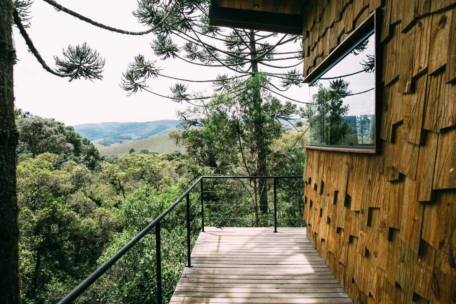 Deck de cabana de madeira com vista para uma exuberante floresta verde e colinas ao longe.