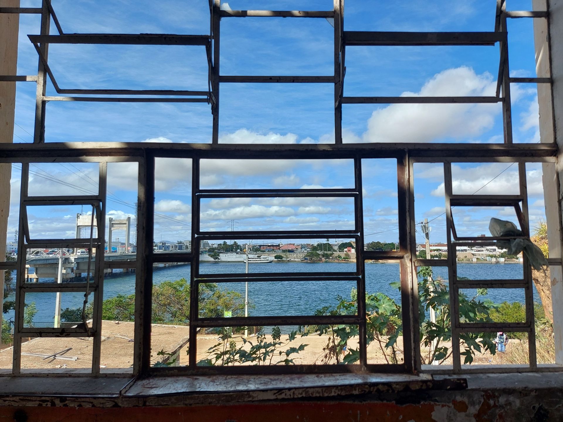 Moldura de janela quebrada com vista para uma baía azul e céu nublado.