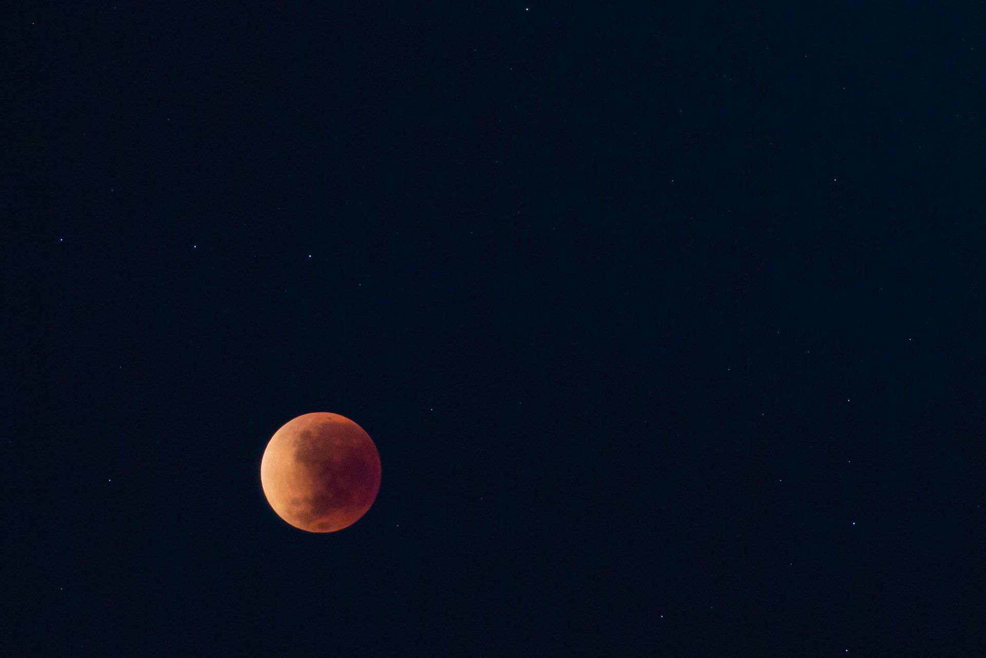 Lua vermelha contra um céu noturno escuro com algumas estrelas tênues.