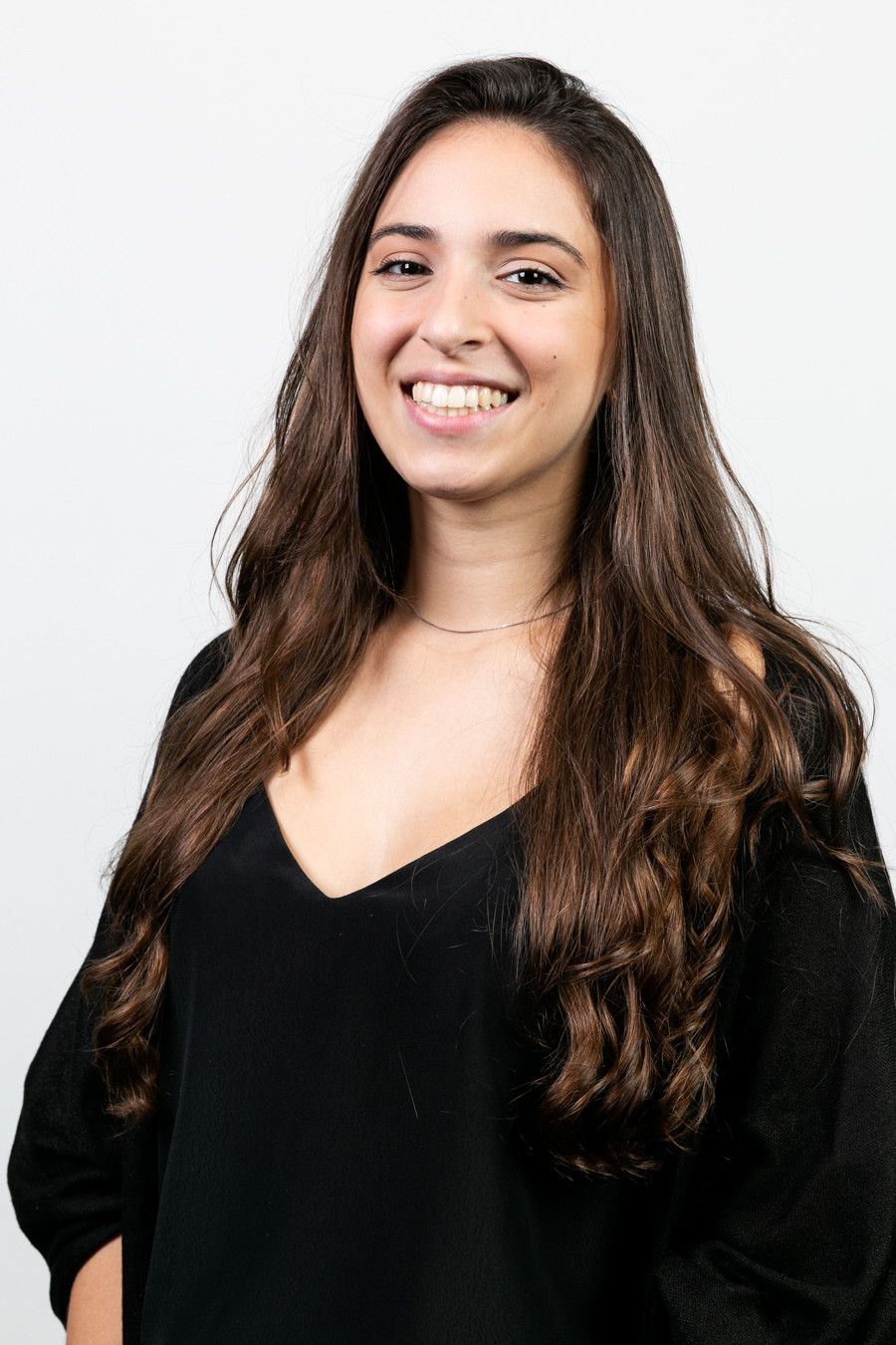 Mulher sorridente com longos cabelos escuros vestindo uma blusa preta contra um fundo branco.