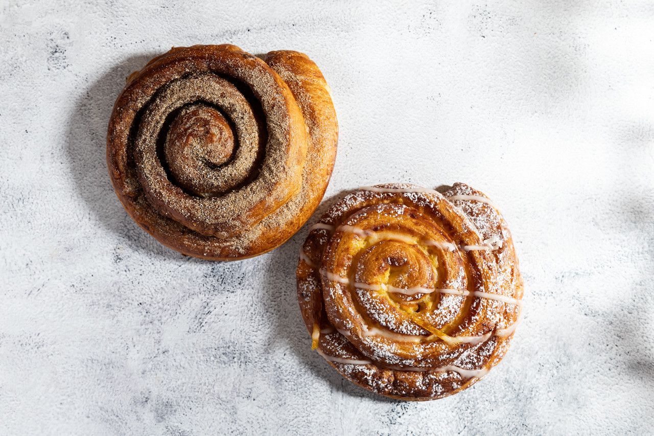 Dois folhados em espiral de canela polvilhados com açúcar de confeiteiro sobre uma superfície cinza clara.